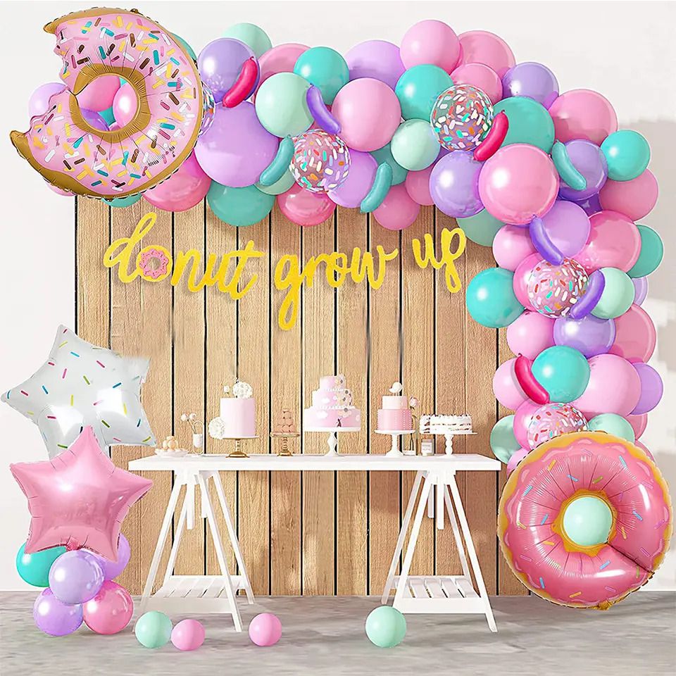 donut grow up balloon arch on wall display with white table and pink cakes 