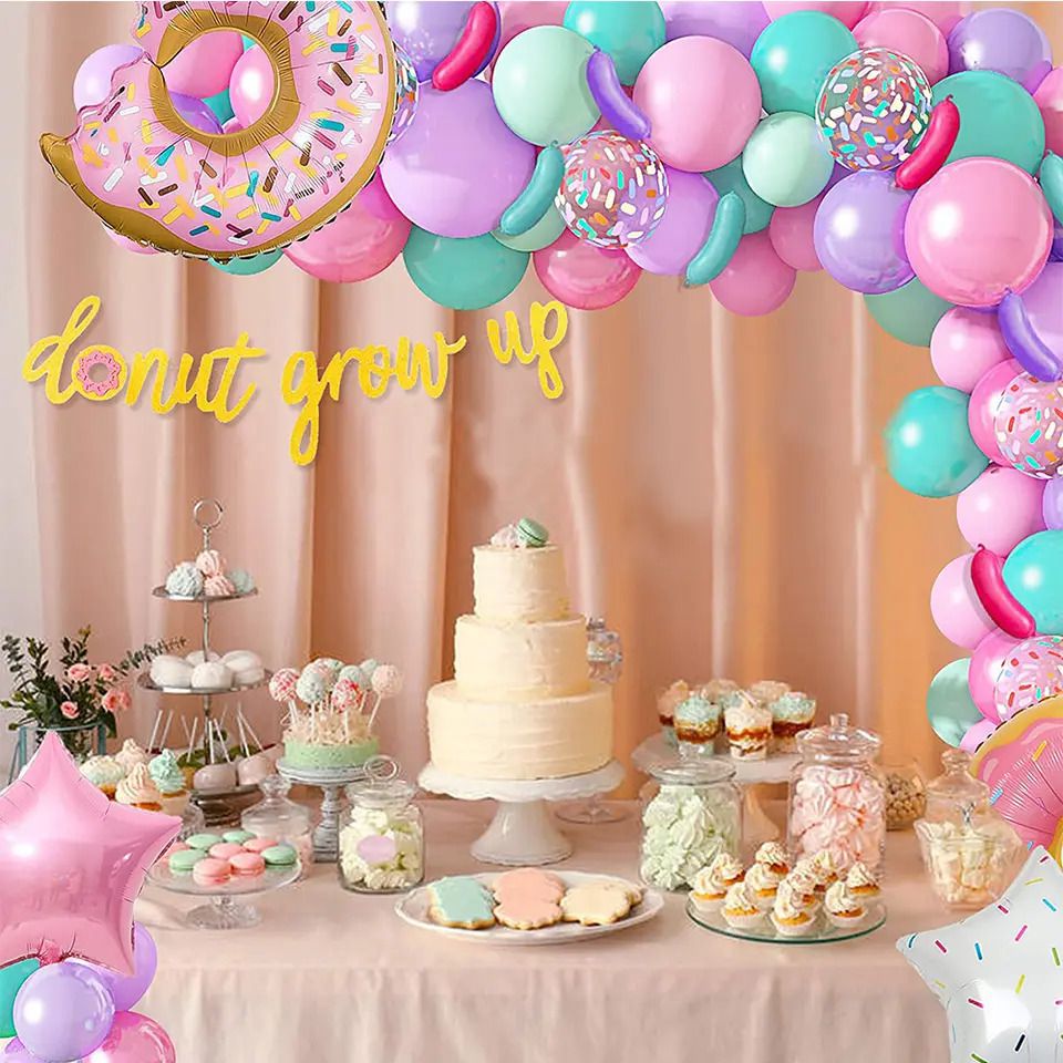 donut grow up balloon arch display on cream wall with table setup cakes and macarons 